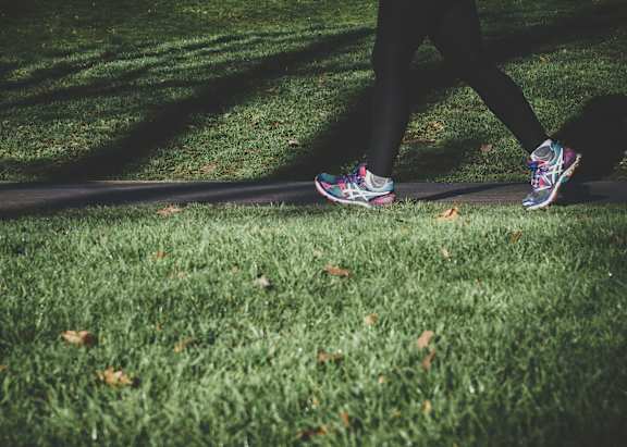 A person is walking on a grassy area with their feet in colorful sneakers.