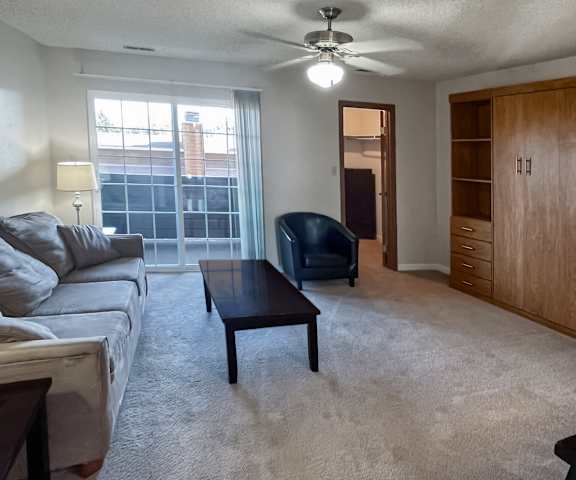 The spacious living room with a couch, plush chairs, coffee table, decorations, an entertainment system, and sliding glass doors to the balcony at Windtree Apartment Homes. 