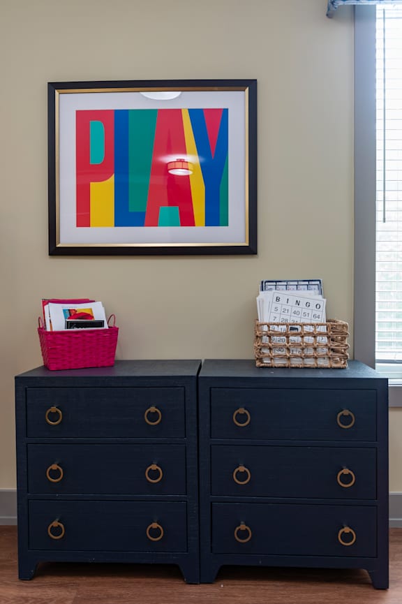 A black dresser with a pink basket on top and a colorful framed artwork above it.