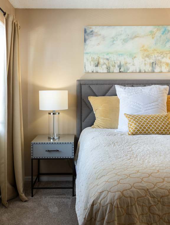 A bedroom with a bed, nightstand, and a painting on the wall.