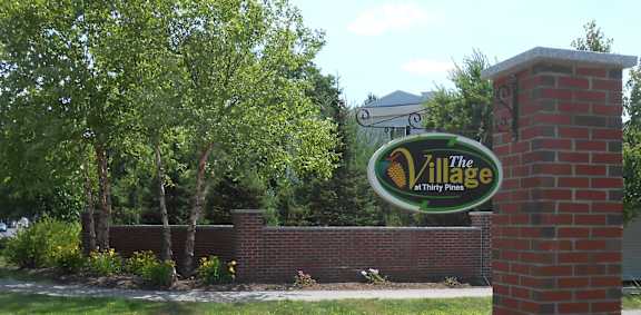 A sign for The Village at Thirty Pines stands in front of a brick wall.