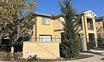 A sign that says Serenity Hills Family Apartments is in front of a building.