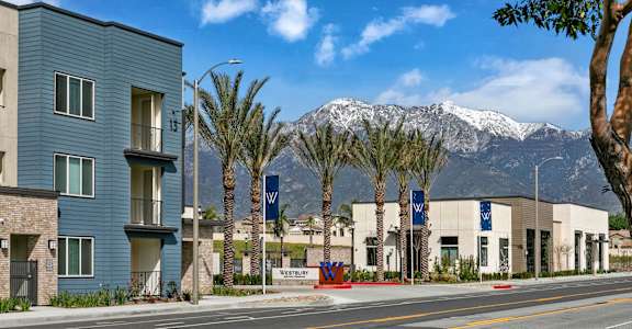 a city street with buildings and palm trees and mountains in the backgroundat Westbury Apartments, Rancho Cucamonga, California