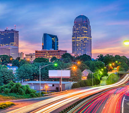 A cityscape at dusk with a prominent building and a highway with light trails.
