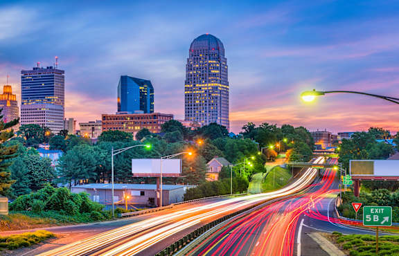 A cityscape at dusk with a prominent building and a highway with light trails.