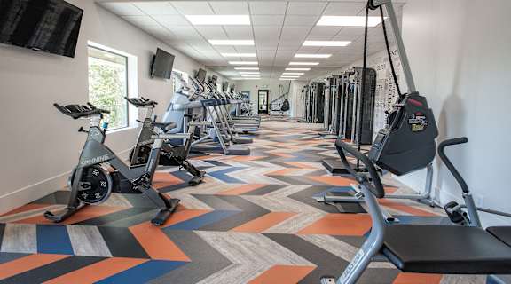 A gym with a variety of exercise equipment including treadmills, stationary bikes, and weight machines.