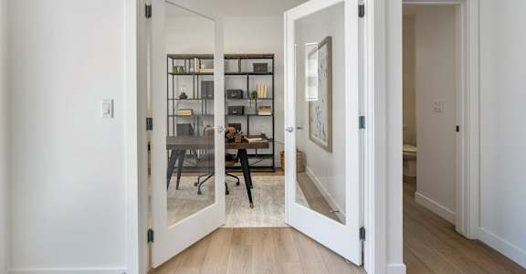A white doorway opens to a room with a desk and chairs.