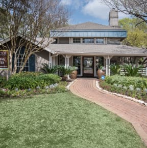 A leasing center for a Polo Club is surrounded by greenery and a brick pathway. at Polo Clubs Apartments, Austin, TX 78729