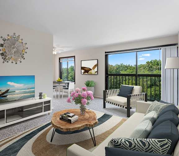 A living room with a television, a sofa, a coffee table, and a balcony with a view of the trees.