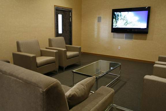 A living room with a glass coffee table and a television mounted on the wall.