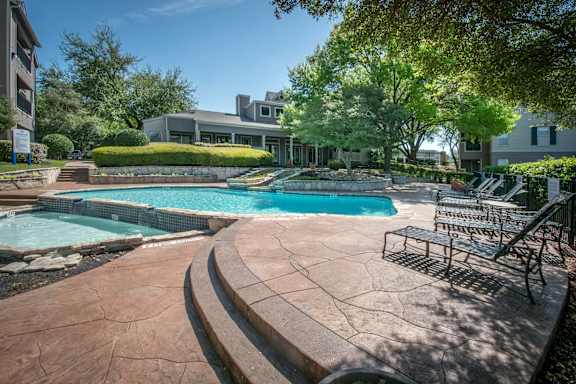 A pool with a stone patio and a house in the background.