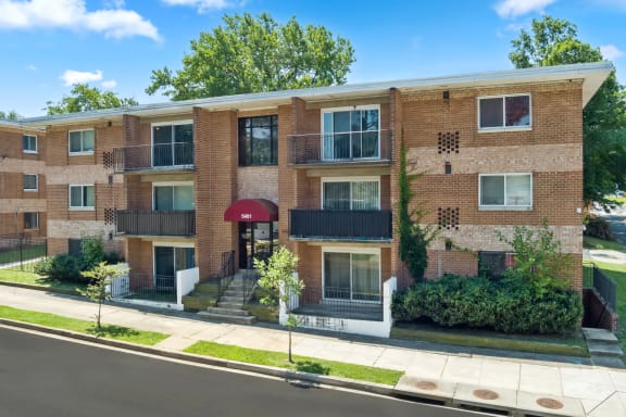 a brick apartment building with a red awning and trees in the background