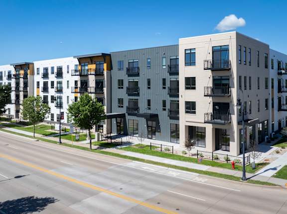 A row of modern apartment buildings line a tree-lined street.