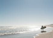 Thumbnail 2 of 4 - a surfer standing on the beach with a surfboard