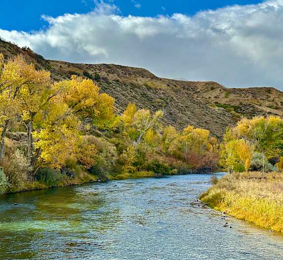 A river flows through a valley with trees in autumn colors.