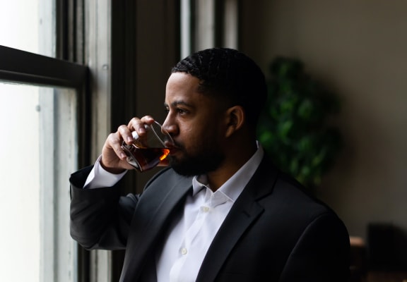 a man in a suit drinking a glass of whiskey