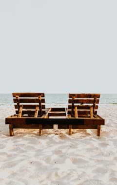 two wooden lounge chairs sitting on the beach
