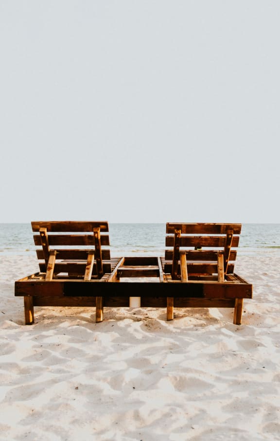 two wooden lounge chairs sitting on the beach