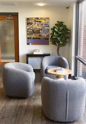 Three grey chairs are arranged around a small table in a room with a large window.