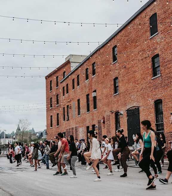 A group of people are dancing in front of a red brick building.