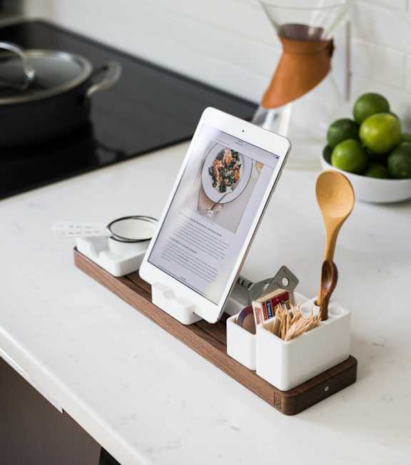 A tablet is on a stand with a bowl of limes and a pot in the background.