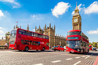 Two red double-decker buses are driving in front of the Big Ben and the Houses of Parliament.