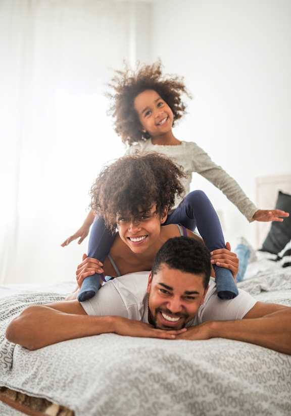 A man is lying on a bed with a child on his back and another child on his shoulders.