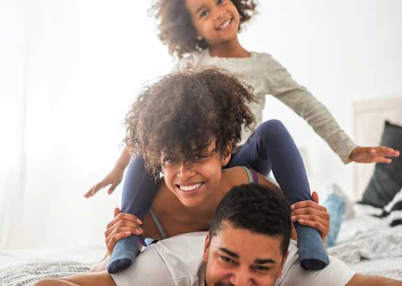A family of three is having fun on a bed.