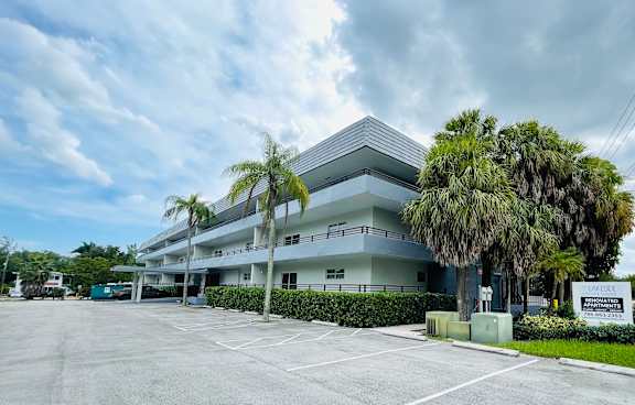 the front of a white house with a yard and a palm tree at Palm Cove Apartments, Daytona Beach Florida