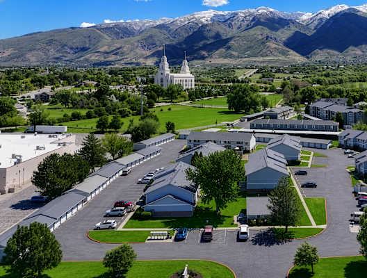 A large white building with a green lawn in front and mountains in the background.