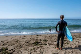 a surfer stands on the beach looking out to the ocean
