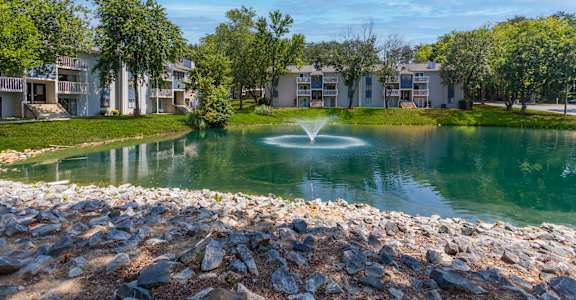 a fountain in the middle of a pond with apartments in the background