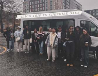 A group of people are standing in front of a white van that says Calico Trip to Cheshire Oaks.