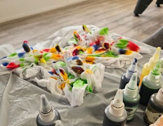 A table covered in a cloth with paint bottles and a palette of paint on it.