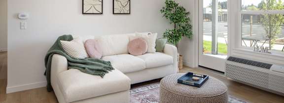 A living room with a grey couch, a wooden chair, and a desk with a plant on it.at The Arvon, Vancouver, WA 98662