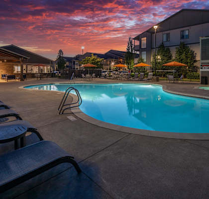 a swimming pool at dusk at an apartment complex with a pink sky