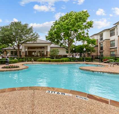 A pool surrounded by trees and a building in the background.