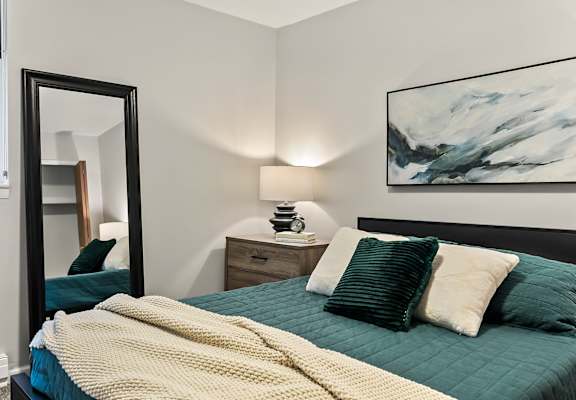 A bedroom with a bed, a nightstand, a mirror, and a painting on the wall.
