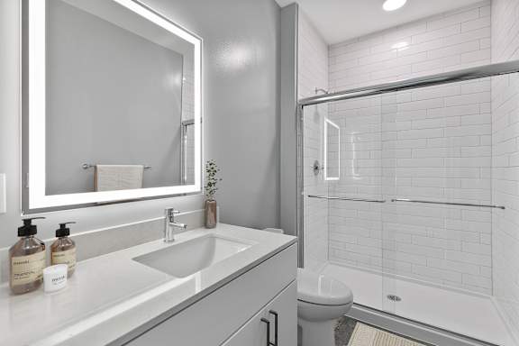 A white bathroom with a sink, mirror, and shower.