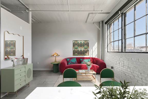 A room with a red couch, green chairs, and a white table.