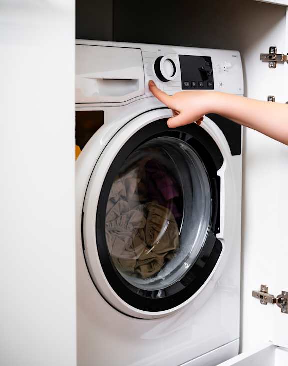 A woman in a yellow outfit is opening a washing machine.