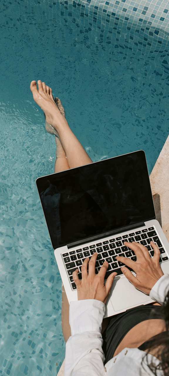 A person is using a laptop with their feet in the water.