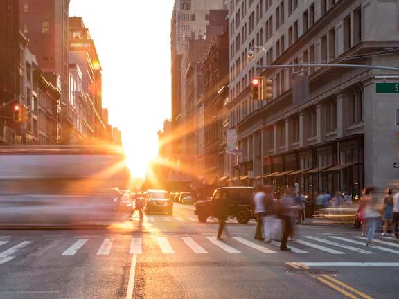 A busy city street at sunset with people crossing the road.