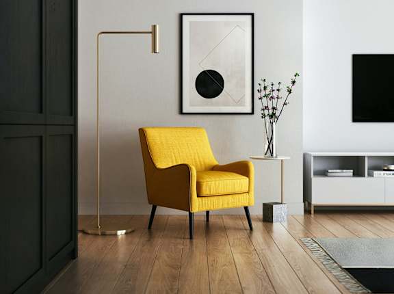 A yellow chair sits in a room with a black and white picture on the wall.