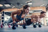 A woman and a man are doing push-ups with kettlebells in a gym.
