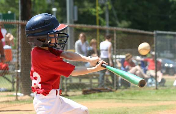 A young boy in a red jersey and blue helmet swings a green bat at a baseball.