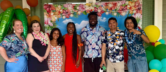 A group of people are standing in front of a floral backdrop with balloons on the sides.