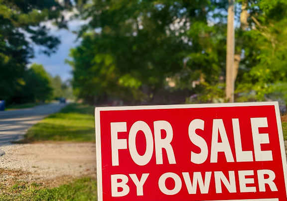 A red and white for sale sign by the roadside.