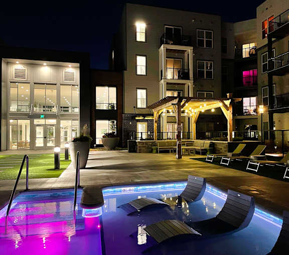 A lit up pool area at night in front of apartment buildings at 42 Hundred On The Lake, St Francis, WI