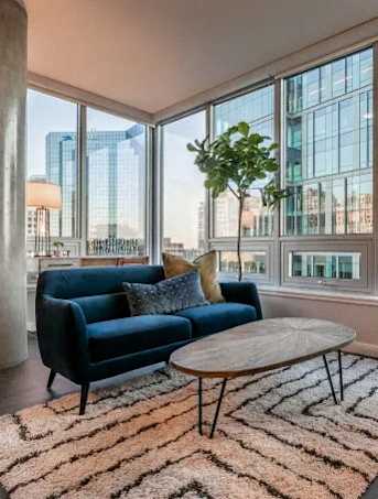A blue couch sits in front of a large window with a view of a city skyline.